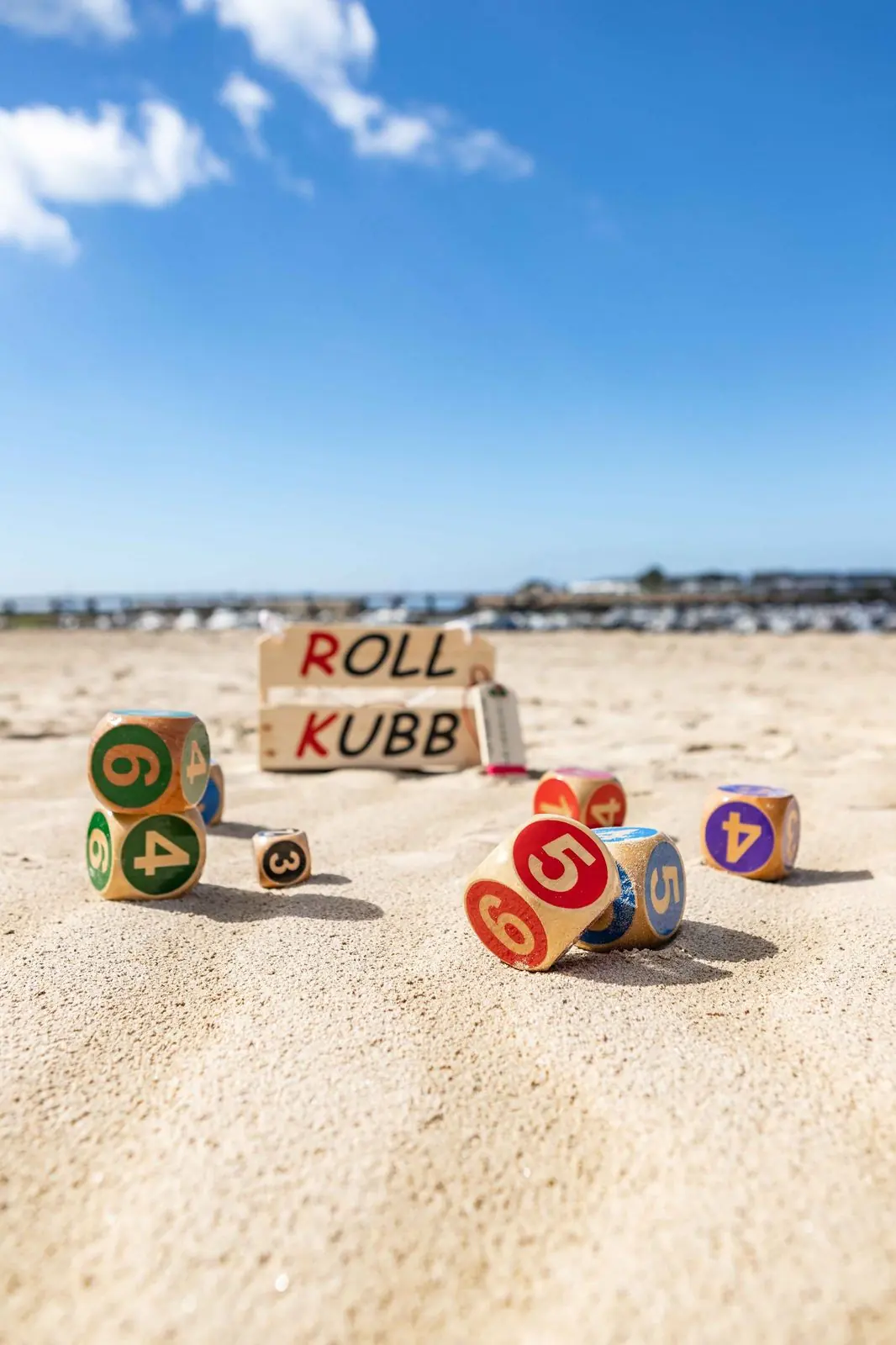 Kubbs numérotés éparpillés sur le sable devant la pancarte Roll Kubb